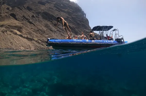 Imagen de la ruta en barco de los Gigantes a Punta Teno con una joven saltando al agua desde el barco